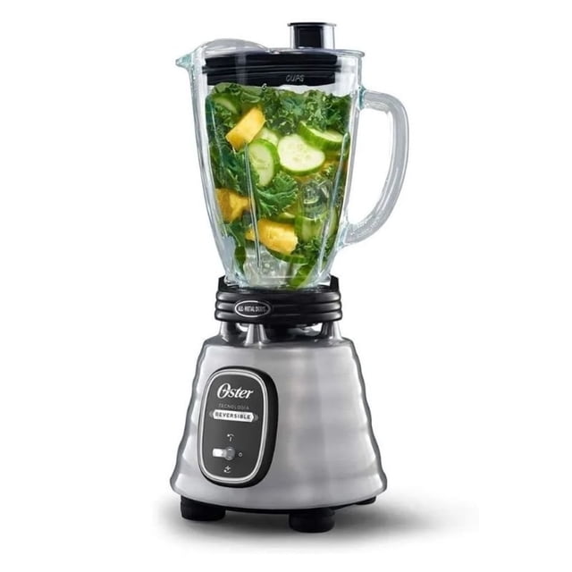 licuadora oster 700w vaso vidrio motor reversible acero inox licuadora frontal con base de acero inoxidable cepillado y jarra refractaria de 1.5 L; interruptor de palanca visible, tapa negra y jarra transparente con frutas y hojas verdes en su interior; diseño profesional con controles ergonómicos; suele usarse para preparar batidos y salsas.