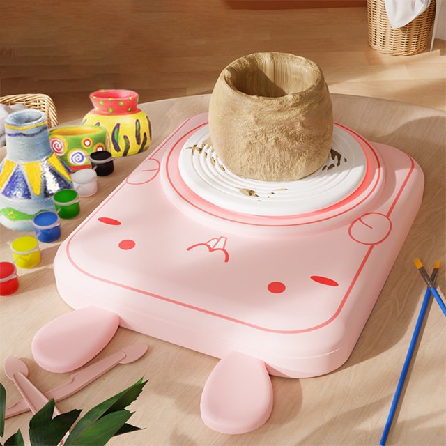 fasiaou pottery wheel for kids: complete pottery kit for beginners with air dry clay - máquina de torno para niños en rosa, vista frontal centrada con una pieza de arcilla sobre la placa giratoria blanca. Base de ABS con esquinas redondeadas, dos almohadillas frontales y controles marcados; incluye herramientas de modelado rosadas, botes de pintura y pinceles sobre mesa de madera. Ideal para manualidades y práctica de modelado para edades 4-8 y 8-12.
