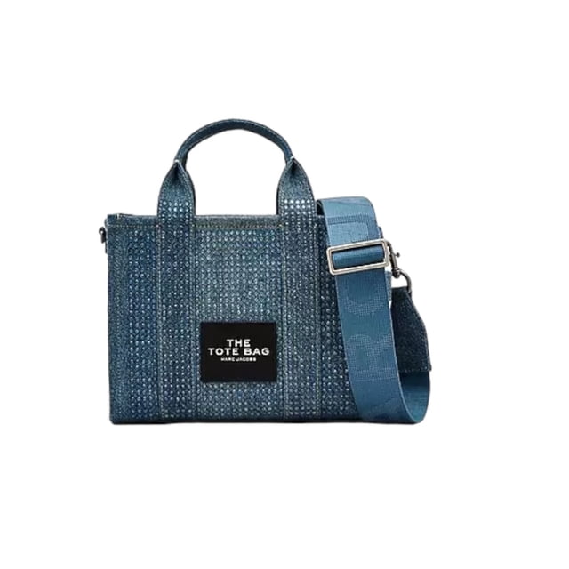 the tote bag marc jacobs crystal denim small mezclilla chica Azul, vista frontal centrada de bolso tote pequeño en mezclilla con cristales transparentes, asas superiores y correa cruzada ancha ajustable y extraíble con hebilla metálica, cierre de cremallera superior y placa frontal negra con texto; interior con forro de sarga y bolsillo deslizante; a menudo usado como bolso cruzado compacto para manos libres.