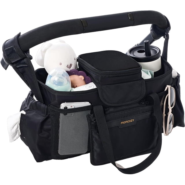 momcozy extra grande max organizador para cochecito - organizador negro compatible con uppababy y doona, vista 3/4 frontal con portavasos térmico que contiene un vaso blanco, bolsillo aislante para chupón hecho con material apto para alimentos y con cremallera, dos compartimentos para biberón (uno con biberón azul), bolsillo de malla con teléfono, cartera pequeña desmontable, asas y correas ajustables para colgar en el manillar y base antideslizante de silicona; también se usa frecuentemente como bolso organizador de viaje para paseos diarios.